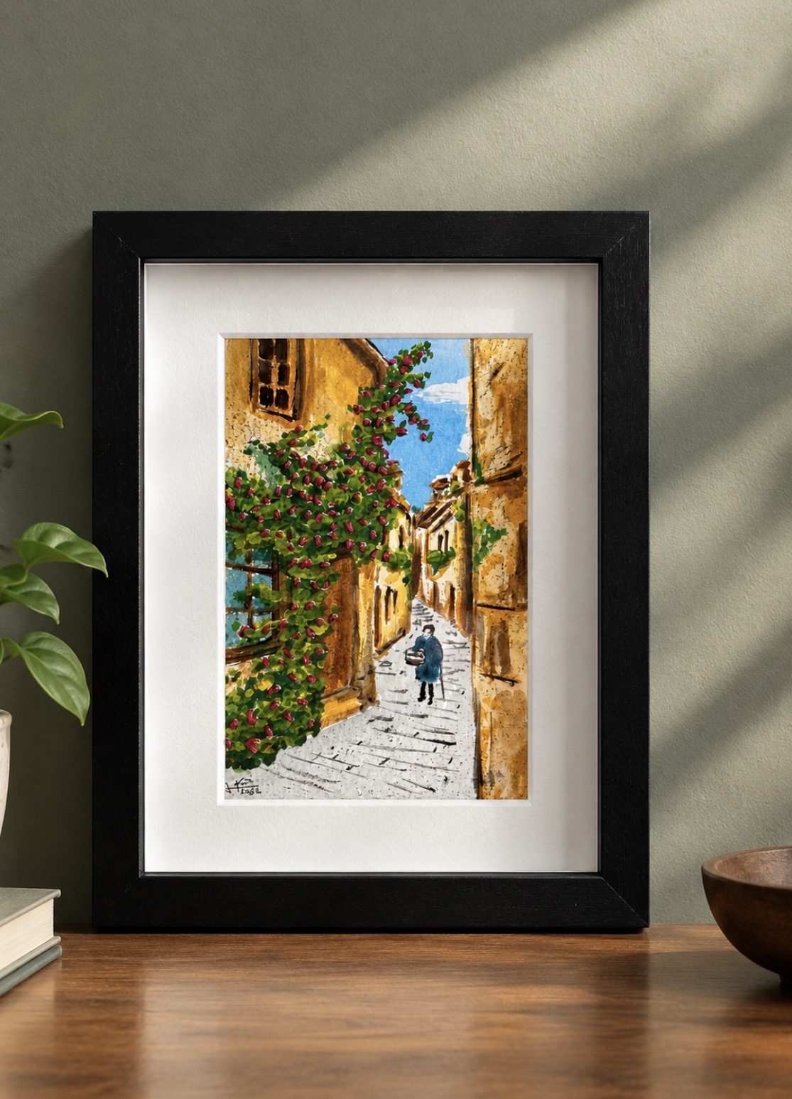 Cuadro de callejón con flores bordadas, marco negro sobre mesa de madera